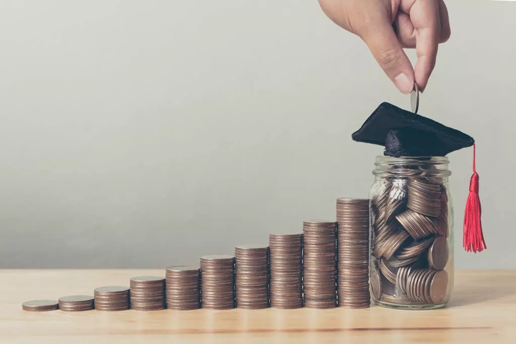 pilhas de moedas com pote de vidro cheio delas e capelo por cima; acima dele, uma m mão coloca uma moeda no pote